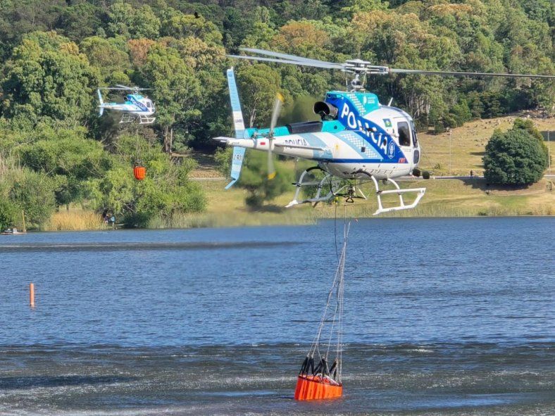 Un helicóptero de la Policía Bonaerense recogue agua del dique de Tandil para combatir las llamas en el Cerro de la Cruz.